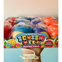 A hand holding a box of colorful Squish Meez Mushi-Pals squishy toys, showing multiple pastel-colored mushroom-shaped squishies wrapped in clear plastic inside a branded box.
