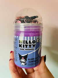 A hand holding a clear plastic tub of Hello Kitty and Friends Slime Pot Surprise purple slime with a clear dome lid and a blue label featuring Kuromi.