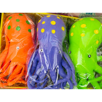 Three octopus-shaped jumbo squishy toys in bright orange, purple, and green, each with yellow polka dots and cartoon eyes, packaged in clear plastic inside a yellow box.