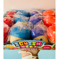A hand holding a box of Squish Mezz Mushtarts, showing several packaged squishy toys in blue, purple, red, and orange. The packaging features a colorful 'Squish Mezz' logo.