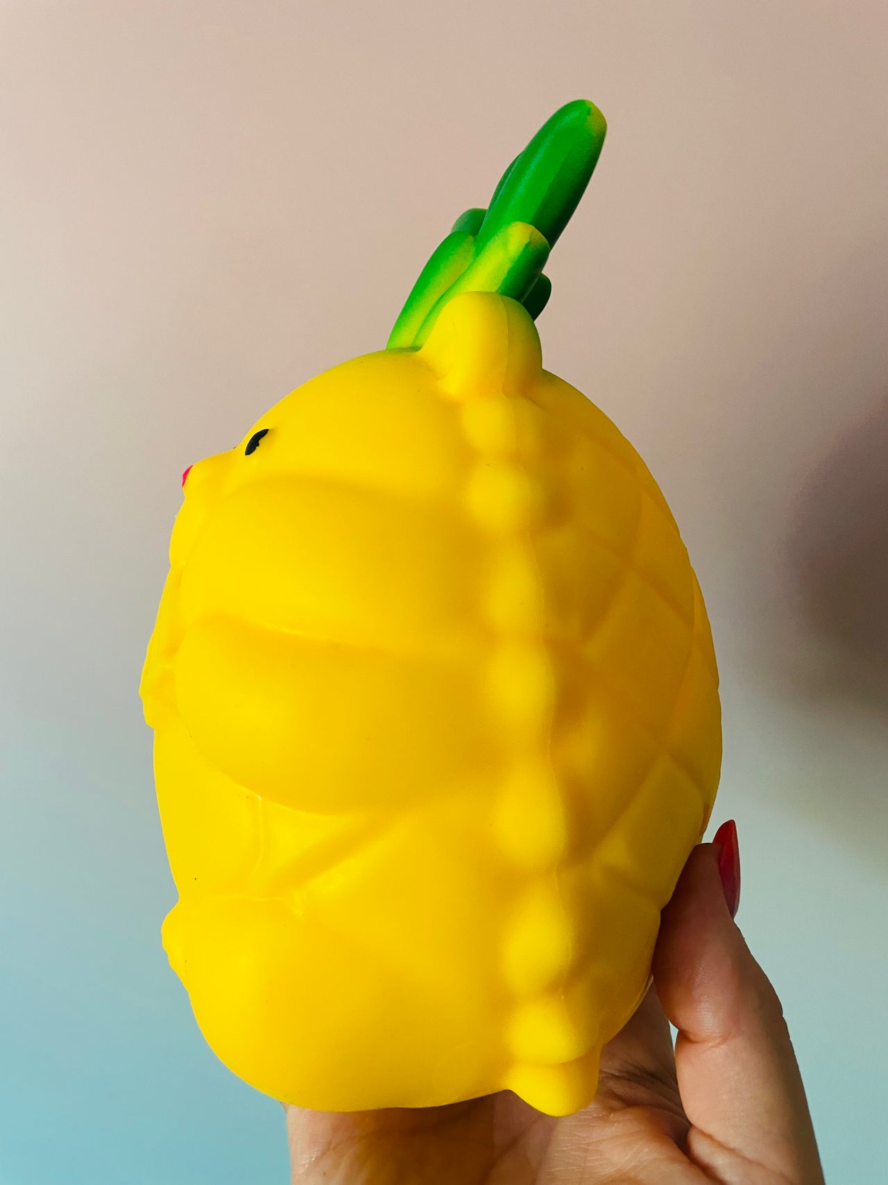 A yellow, pineapple-shaped squishy toy held in a hand against a soft, light-colored background.