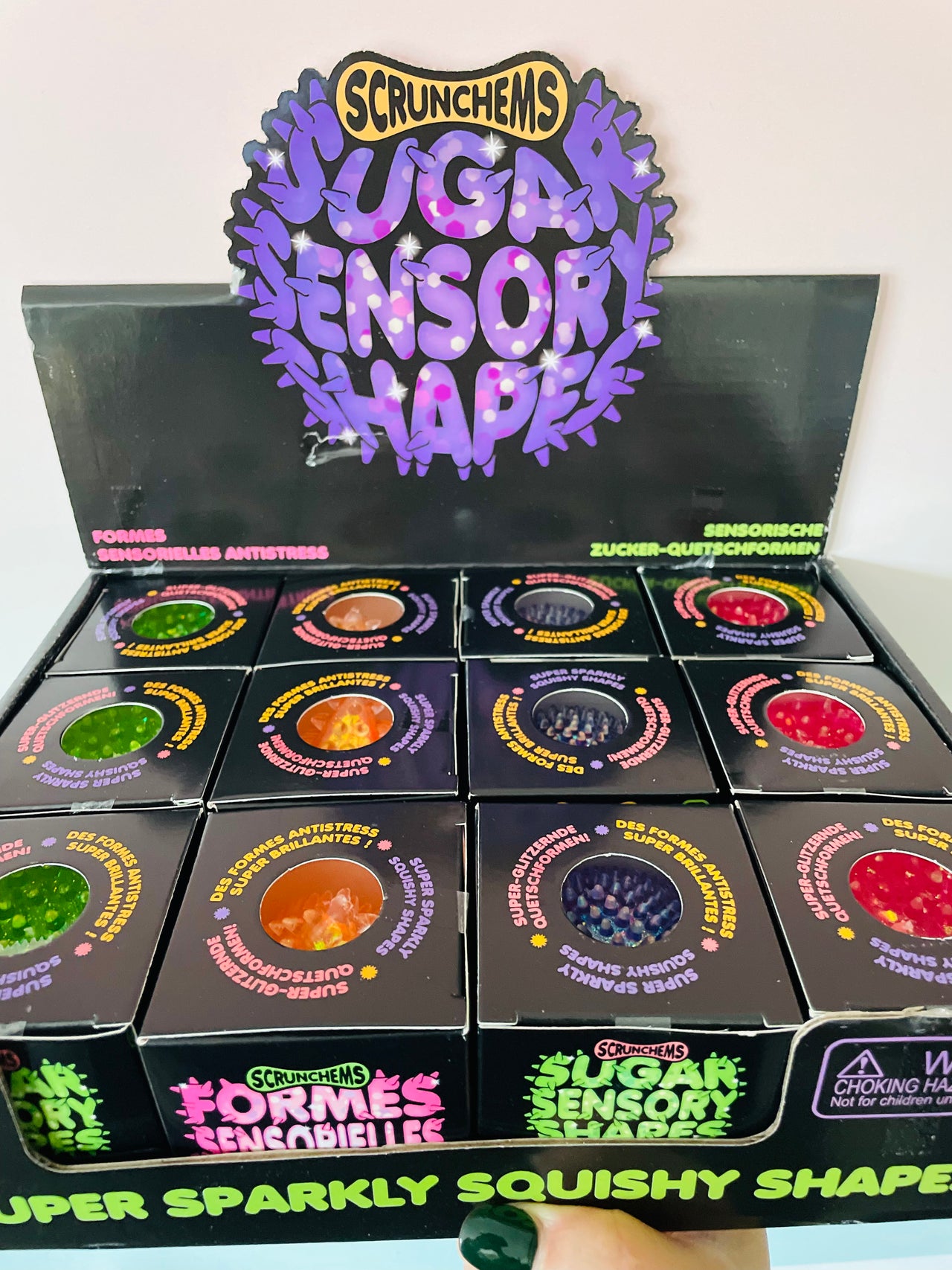 A display box of Scrunchems Sugar Sensory Shapes gummy candies, showing multiple colorful circular gummies in individual boxes beneath a large purple logo sign.