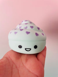 A cute, squishy toy shaped like a cupcake with purple hearts on the frosting and a smiling face, held in a person's hand against a soft pink background.